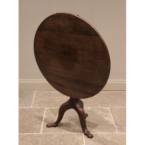 757 - A George III oak tilt-top tripod table, the circular plank top raised upon a ring turned gun barrel ... 