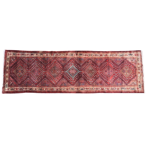 618 - A large terracotta ground Persian runner, in red, blue and ivory colourways, the seven lozenge shape... 