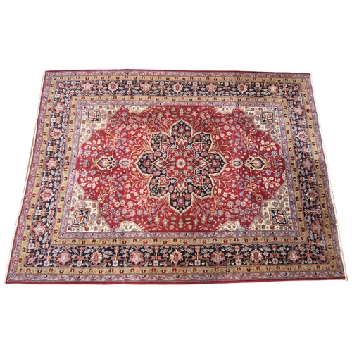 621 - A large deep red ground Persian carpet, the central floral medallion enclosed by conforming spandrel... 