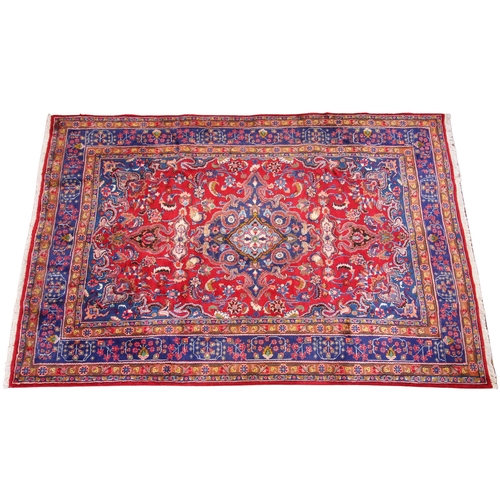 622 - A red ground Persian Mashad carpet, the central blue medallion upon a trailing ground enclosed by sp... 