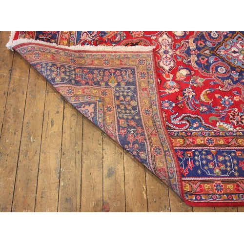 622 - A red ground Persian Mashad carpet, the central blue medallion upon a trailing ground enclosed by sp... 