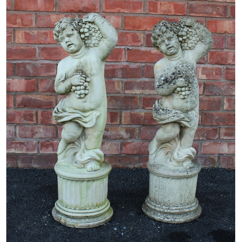 548 - A pair of reconstituted stone cherubs, each modelled arm raised holding fruit, upon an integrated fl... 