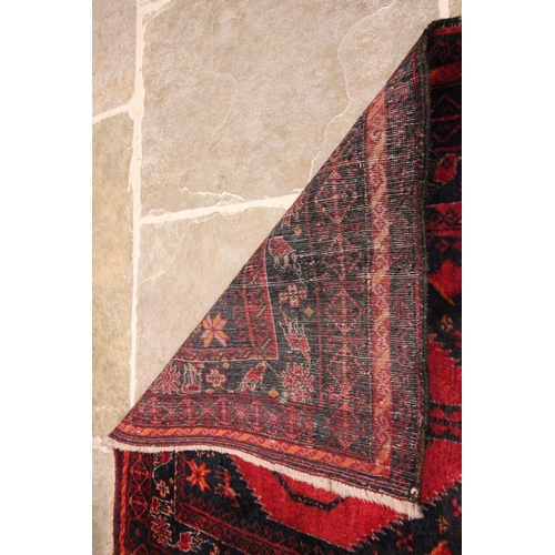 615 - An Afghan wool rug, in red and blue colourways, the three central hexagonal red medallions on a blue... 