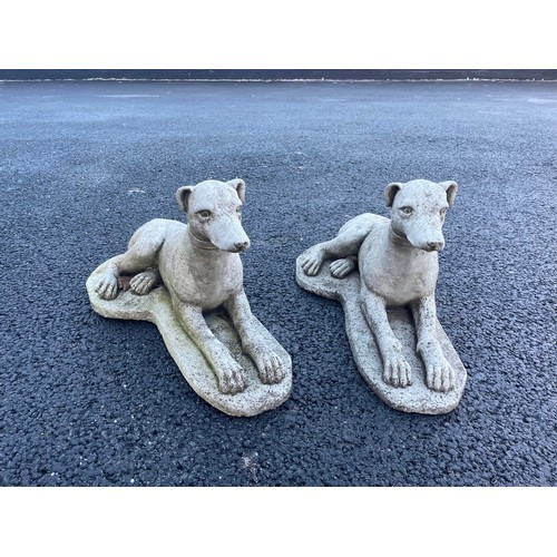 553 - A pair of reconstituted stone garden ornaments, each modelled as a recumbent whippet upon an integra... 