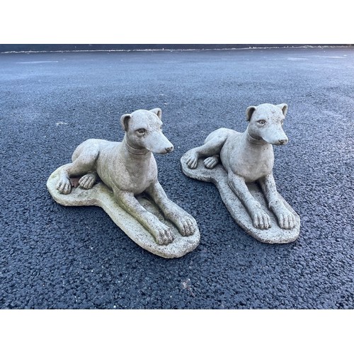 553 - A pair of reconstituted stone garden ornaments, each modelled as a recumbent whippet upon an integra... 