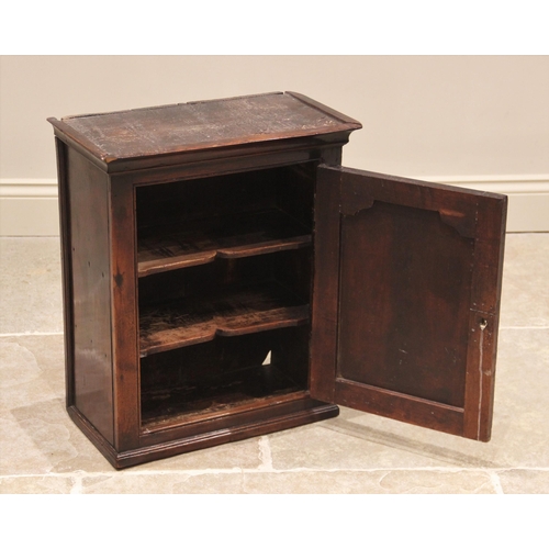 626 - An 18th century oak spice cupboard, the moulded cornice above a single panelled door opening to two ... 