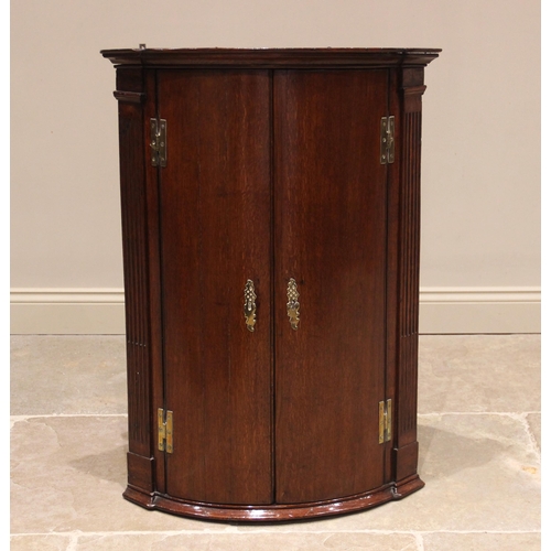 640 - A George III oak bowfront hanging corner cupboard, the moulded cornice over a pair of convex doors m... 