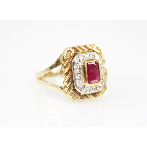 211 - A ruby and diamond cluster ring, the central emerald cut ruby measuring 6mm x 3.5mm, set to a surrou... 