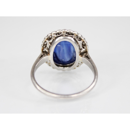 192 - An early 20th century sapphire and diamond cluster ring, the central oval sapphire cabochon measurin... 