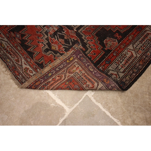 587 - A Caucasian wool rug, in red and black colourways, the central field with four linked geometric meda... 