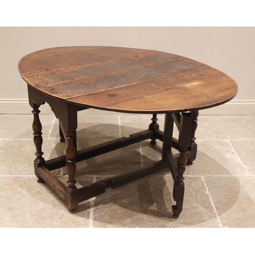 648A - An 18th century oak drop leaf table, the oval top above a shaped frieze upon baluster and inverted b... 