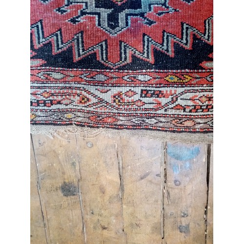 587 - A Caucasian wool rug, in red and black colourways, the central field with four linked geometric meda... 