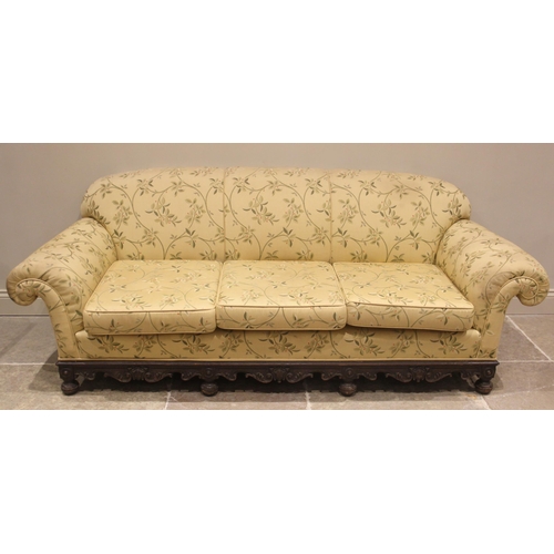 825 - A Victorian carved oak sofa, later re-upholstered in foliate fabric, the scalloped padded back rest ... 