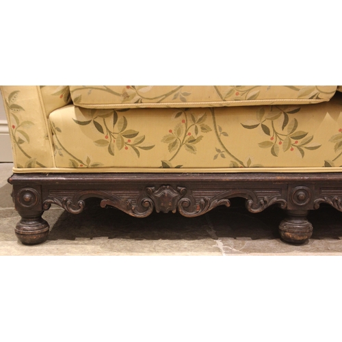 825 - A Victorian carved oak sofa, later re-upholstered in foliate fabric, the scalloped padded back rest ... 