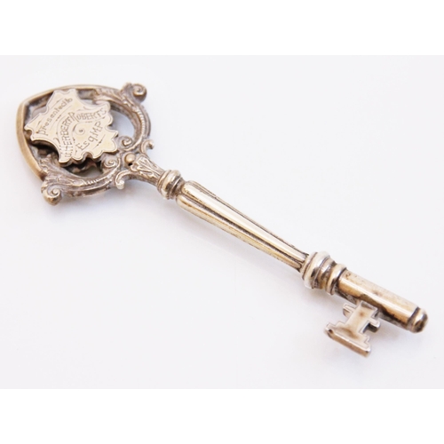 93 - A silver coloured presentation key, the key with two cartouches within an openwork scroll border,  e... 