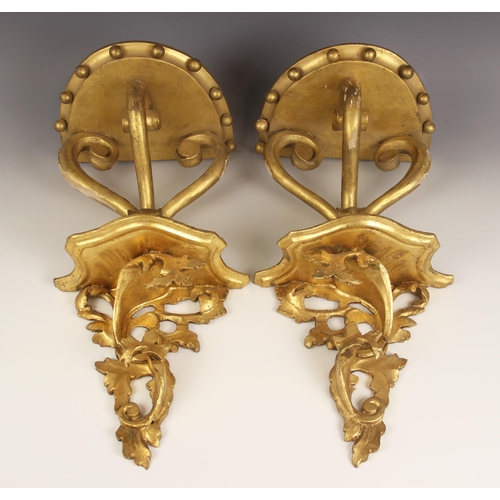 673 - A pair of giltwood rococo wall brackets, each with a shaped moulded shelf upon scroll acanthus suppo... 