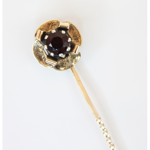 183 - A garnet set yellow metal stick pin, the round cut garnet cut down set within a flower head designed... 