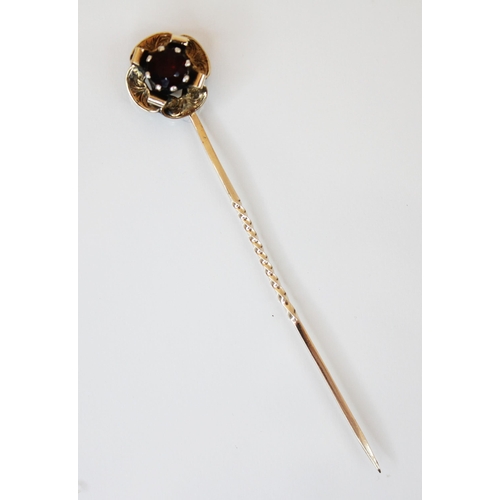 183 - A garnet set yellow metal stick pin, the round cut garnet cut down set within a flower head designed... 