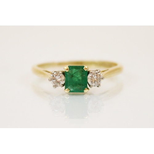 235 - A diamond and emerald 18ct gold three stone ring, the central rectangular cut emerald with round cut... 