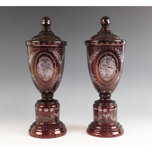 532 - A pair of Bohemian ruby flashed glass urns and covers, each extensively wheel cut with floral and fo... 