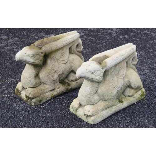 712 - A pair of reconstituted stone garden ornaments, modelled as recumbent griffins with wings closed, up... 