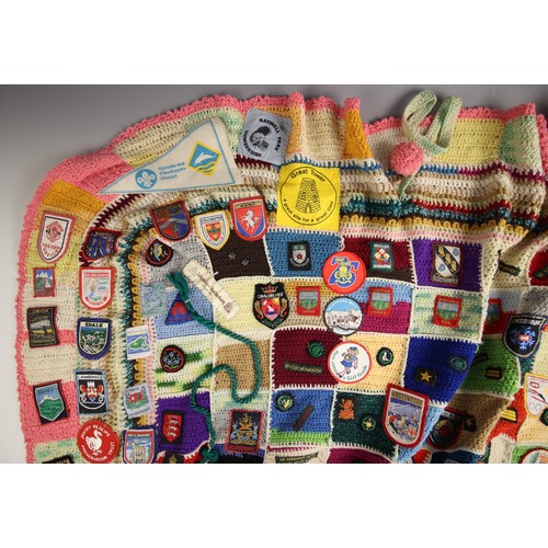 558 - SCOUTS/GUIDES INTEREST: A crocheted patchwork fireside blanket, late 20th century, extensively appli... 