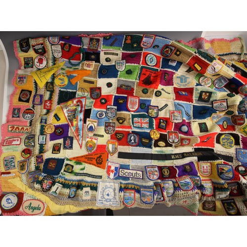 558 - SCOUTS/GUIDES INTEREST: A crocheted patchwork fireside blanket, late 20th century, extensively appli... 