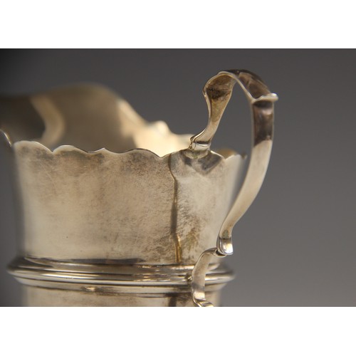 91 - A George V silver cream jug, Wakely & Wheeler, Dublin 1912, in Georgian style, with scroll handle an... 