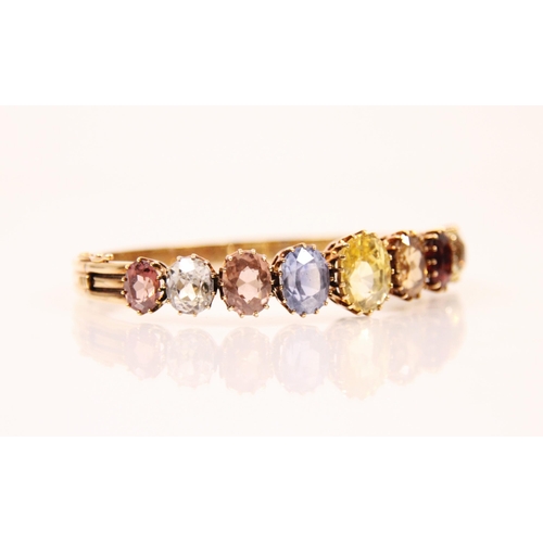 123 - An early 20th century multi gemstone graduated bangle, the central oval cut yellow sapphire with fou... 