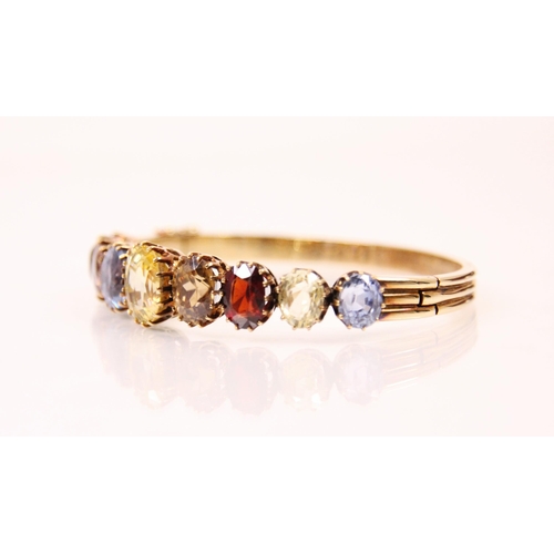 123 - An early 20th century multi gemstone graduated bangle, the central oval cut yellow sapphire with fou... 