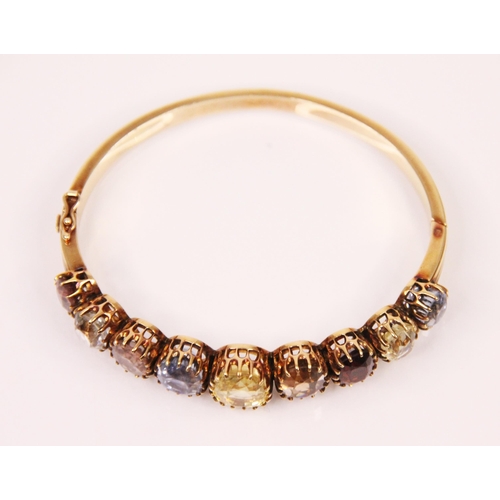 123 - An early 20th century multi gemstone graduated bangle, the central oval cut yellow sapphire with fou... 