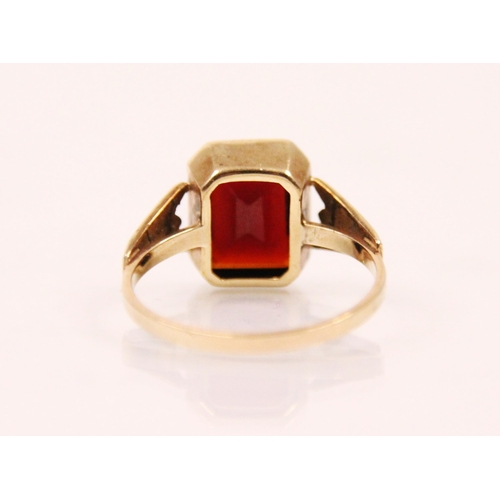 125 - A garnet and 9ct gold ring, the emerald cut garnet within a milgrain setting edge, leading to tapere... 