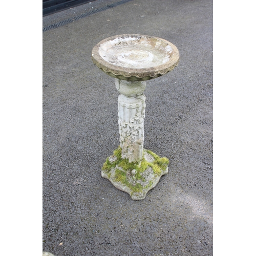 814 - A reconstituted stone bird bath, the shallow circular well upon a fluted pedestal, cast in relief wi... 