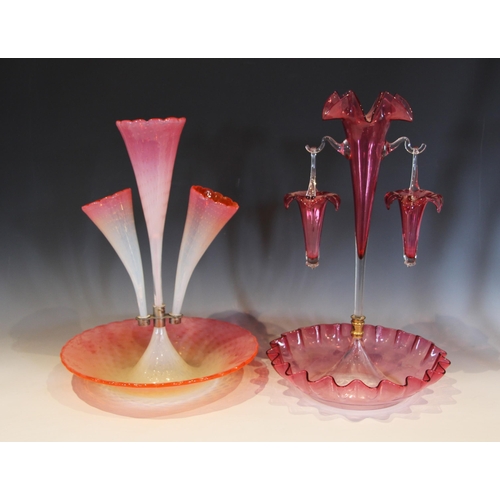 493 - A cranberry glass epergne, with a central trumpet supporting two hanging baskets, each rim modelled ... 