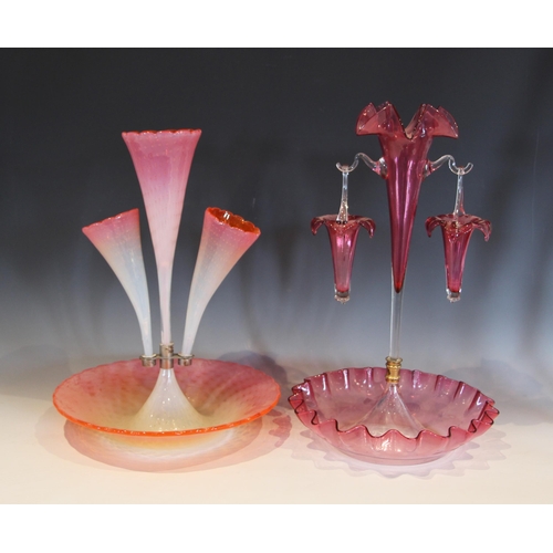 493 - A cranberry glass epergne, with a central trumpet supporting two hanging baskets, each rim modelled ... 