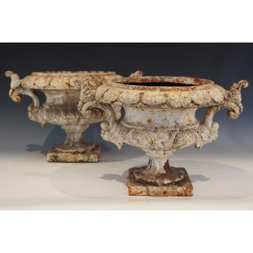 620 - A pair of Victorian cast iron Warwick type urns, each white painted and raised on an integral square... 