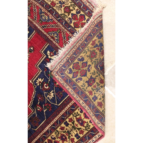 1052 - A Persian pattern wool carpet, in red, blue and ivory colourways, the central angular medallion with... 