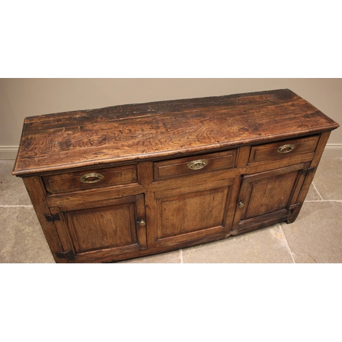 1100 - An early 18th century elm dresser base, the figured and moulded, oversailing top above an arrangemen... 