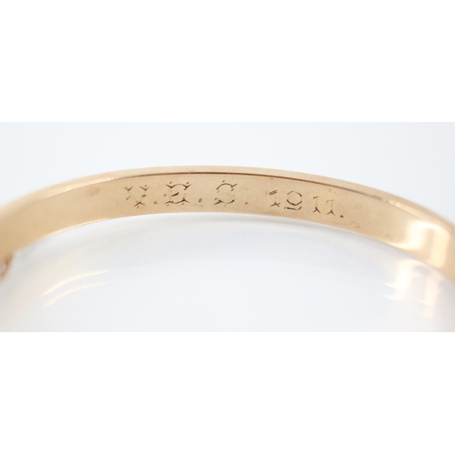 245 - An Edwardian yellow metal bangle, the plain polished bangle with overlay shaped detail, engraved to ... 