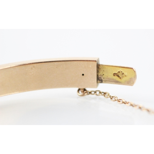 245 - An Edwardian yellow metal bangle, the plain polished bangle with overlay shaped detail, engraved to ... 