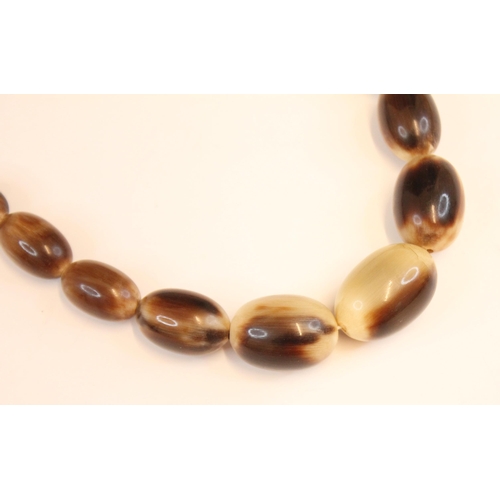 173 - A graduated carved and polished horn bead necklace, each bead of elongated oval form, with screw cla... 