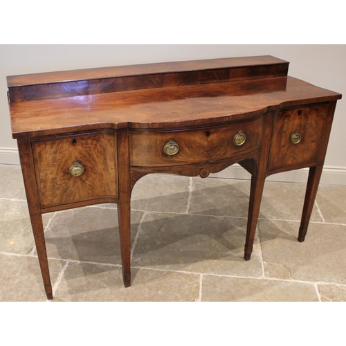 1025 - A George III mahogany sideboard, the stepped back over a break arch shaped top, a central crossbande... 