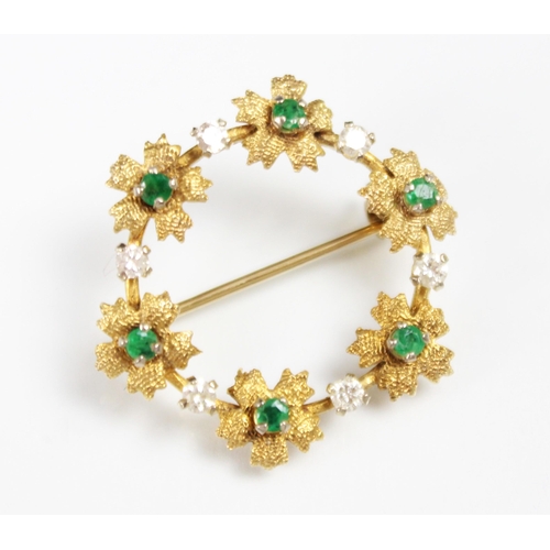 311 - A 9ct yellow gold emerald and diamond set brooch, the circular brooch with six textured flowerhead d... 