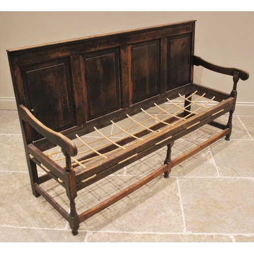 1006 - A George III oak settle, the four panel back extending to down swept arms, over the rope work seat w... 