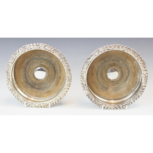 102 - A pair of silver plate bottle coasters, the circular cast rim with scrolling leaf design above a pla... 