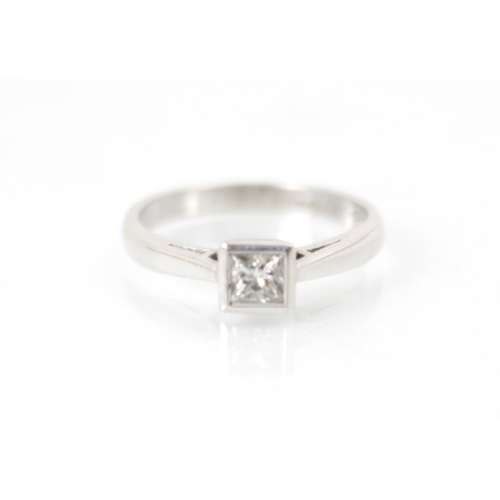 247 - A square cut diamond solitaire ring, the diamond within a white metal rub over setting edge, leading... 