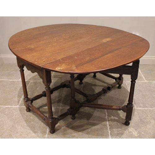 970 - An 18th century oak drop leaf dining table, the oval top over a shaped apron upon ring turned taperi... 