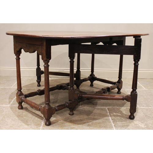 970 - An 18th century oak drop leaf dining table, the oval top over a shaped apron upon ring turned taperi... 