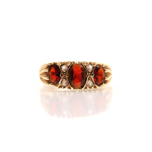 287 - A late 20th century garnet ring, the central oval cut garnet with smaller oval cut garnet to each si... 