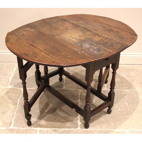 988 - An 18th century oak gateleg table, the oval plank top over a single frieze drawer, upon slender balu... 